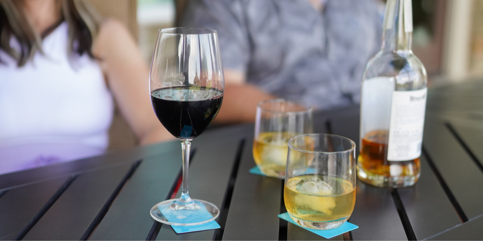 Wine glasses with different types of wine on a table with people in the background with their drinks sitting on BOCE coaster card