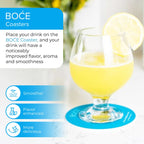 A glass of yellow drink with a lemon slice sits on a bright blue BOĆE Coaster. Text highlights the product’s benefits: smoother taste, enhanced flavor, and more delicious aroma. The background shows a light, modern kitchen with soft natural lighting.