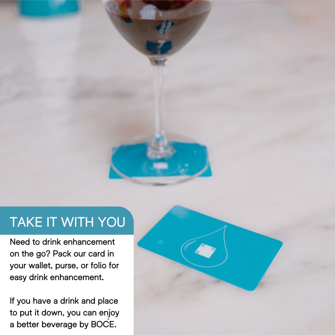 Wine glass resting on a blue BOĆE card with another card nearby, showing portability and simple use for drink enhancement.