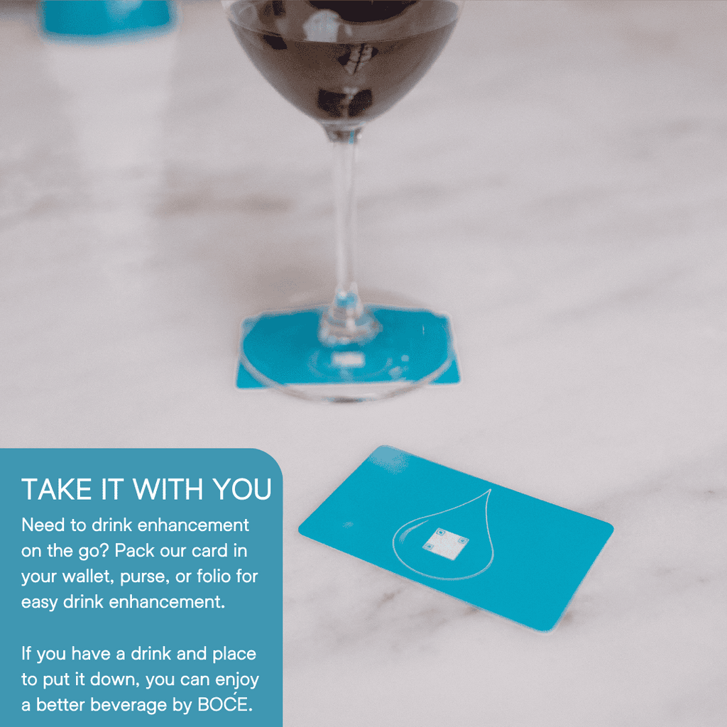 Wine glass resting on a blue BOĆE card with another card nearby, showing portability and simple use for drink enhancement.