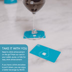 Wine glass resting on a blue BOĆE card with another card nearby, showing portability and simple use for drink enhancement.