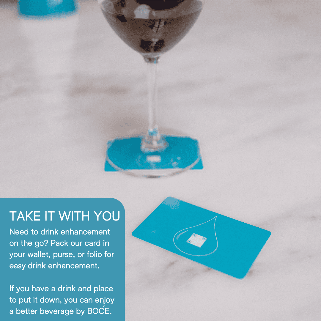 Wine glass resting on a blue BOĆE card with another card nearby, showing portability and simple use for drink enhancement.