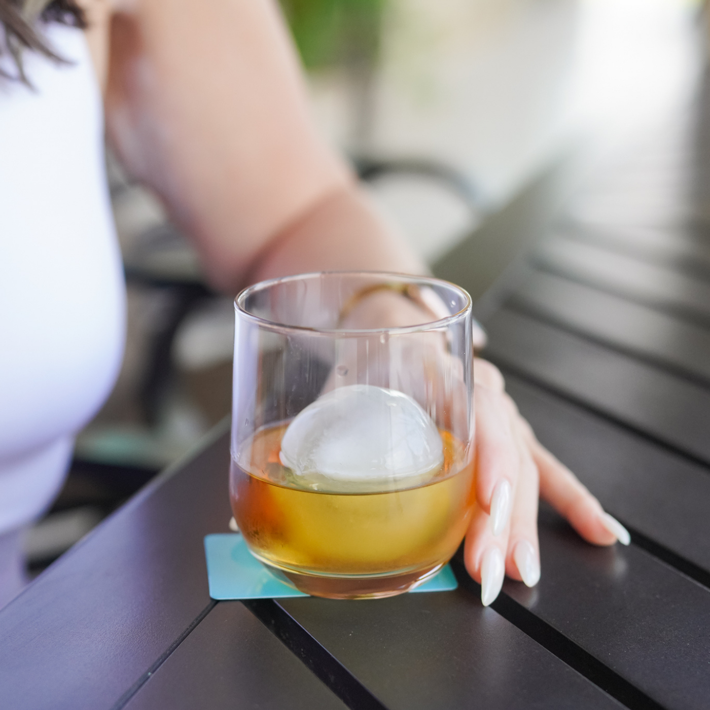 Glass of bourbon with a white ice cube on a table, blurred background