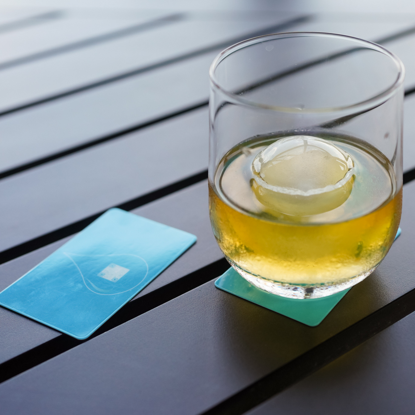 Glass of yellow liquid with a lemon slice on a wooden table with on BOCE blue card coasters.